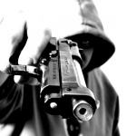 Парень в капюшоне держит в руке пистолет закрывающий его лицо