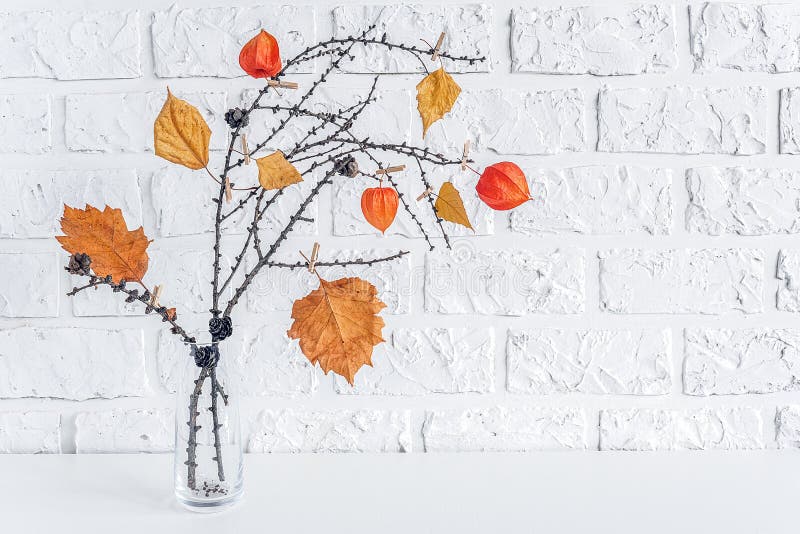 Autumn creative bouquet of branches with yellow leaves on clothespins in vase on table background white brick wall Copy space stock image