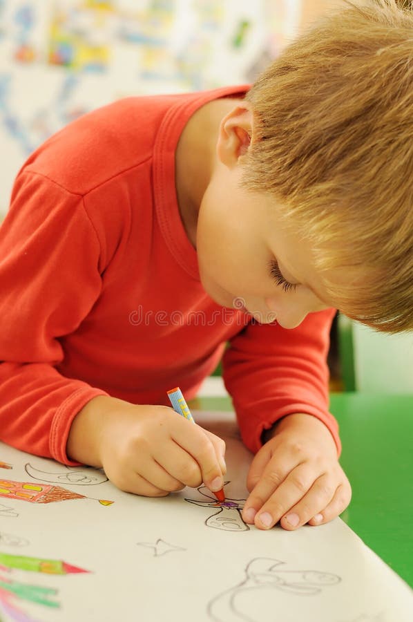 Child drawing. Young child sitting behind a table and drawing a picture on the paper stock image