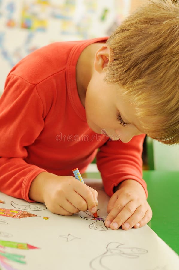 Child drawing. Young child sitting behind a table and drawing a picture on the paper stock image Child drawing. Young child sitting behind a table and drawing a picture on the paper stock image