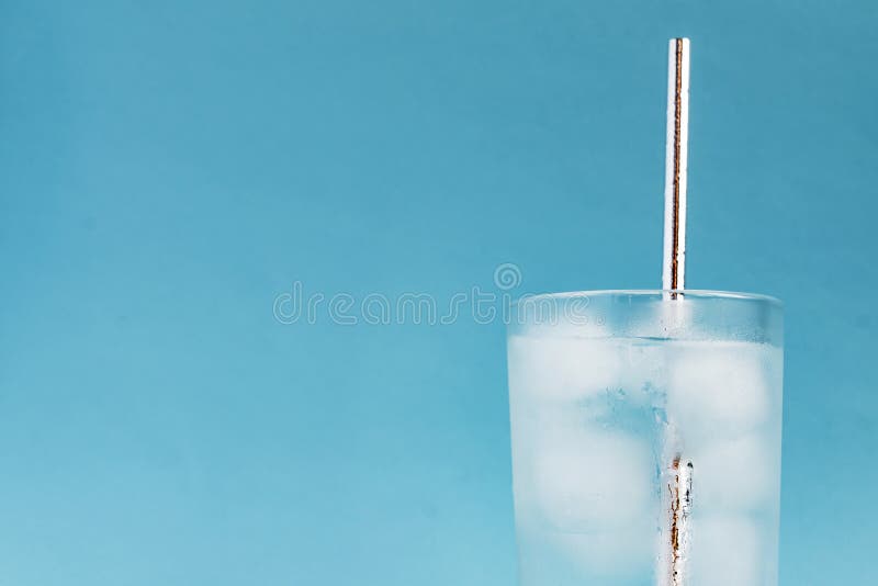 Close up of pure water with ice and silver paper straw in tall transparent glass and sun glare on blue background. Copy space. stock image Close up of pure water with ice and silver paper straw in tall transparent glass and sun glare on blue background. Copy space. stock image
