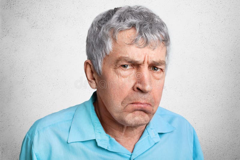 Displesed unhappy wrinkled mature male frowns face and curves lips, wears formal shirt, poses against white concrete background. C. Lose up of elederly man royalty free stock photography