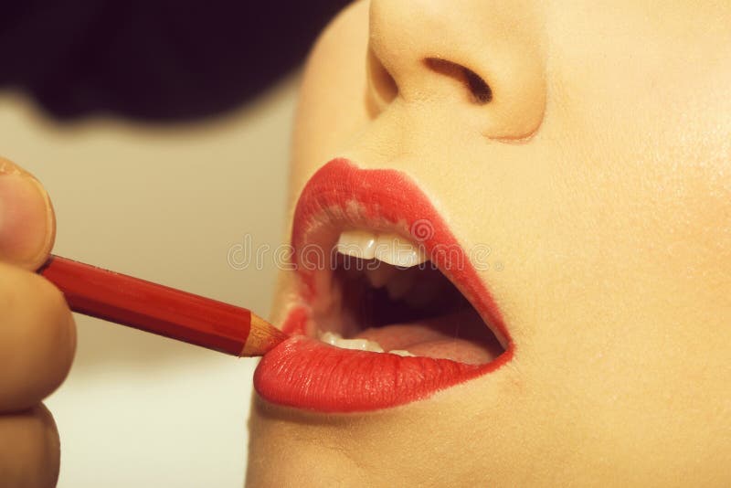 Lips getting red pencil makeup by male hand. Open mouth with white healthy teeth on female face. Young facial skin. Visage, make up and skincare. Beauty salon stock images