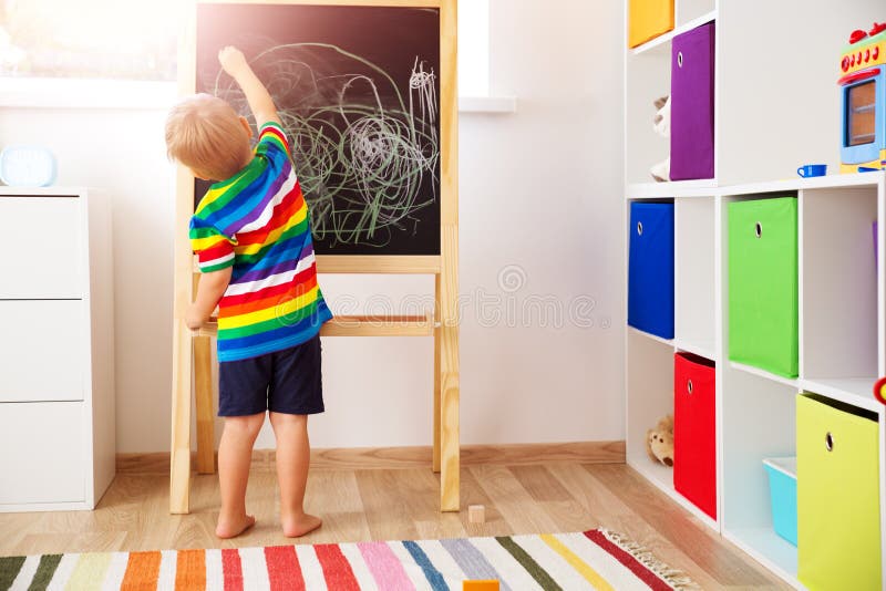 Little child drawing on the blackboard. Boy standing in the room with chalkboard stock image