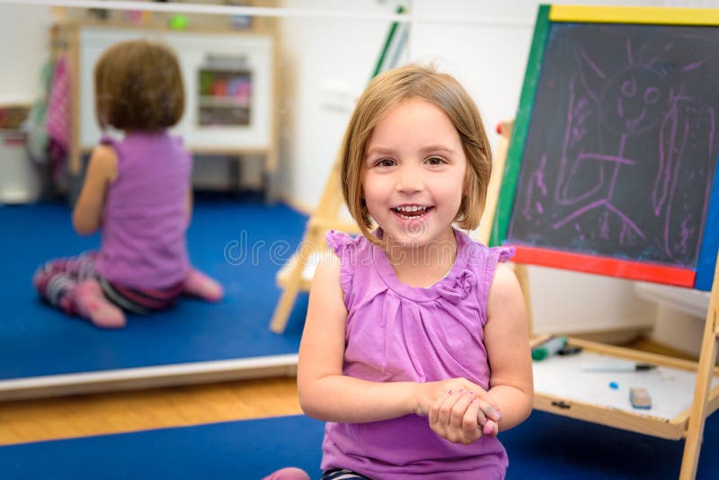 Little child is drawing with color chalk on the chalk board. Little child is drawing with pieces of color chalk on the chalk board. Girl is expressing creativity stock photo