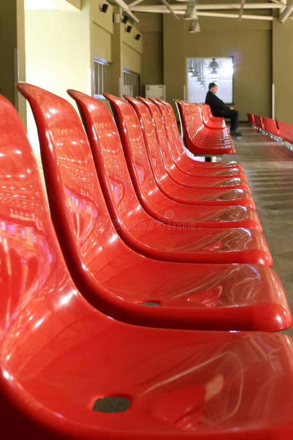 Lonely man is sitting on the last chair in the empty row of red chairs. Perspective, window royalty free stock photography Lonely man is sitting on the last chair in the empty row of red chairs. Perspective, window royalty free stock photography