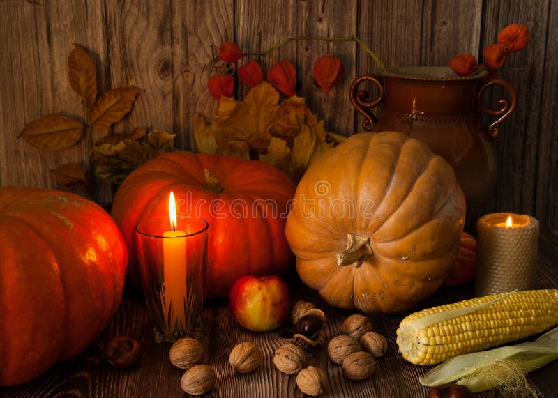 Orange pumpkins, burning candles, walnuts and chestnuts, corn, physalis, ceramic vase, autumn leaves on a wooden background. royalty free stock photos
