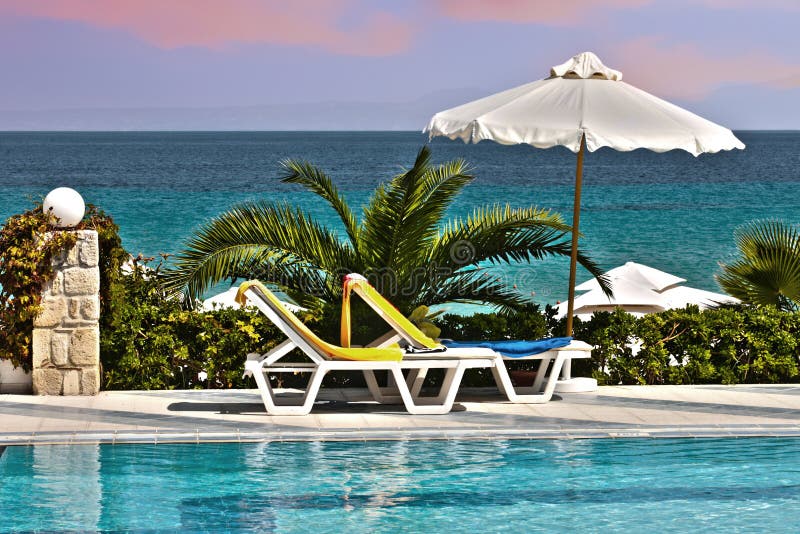 Plastic chair beside the pool with a perspective close to the sea. Relaxing Tanning beds beside swimming pool on remote beach royalty free stock photography Plastic chair beside the pool with a perspective close to the sea. Relaxing Tanning beds beside swimming pool on remote beach royalty free stock photography