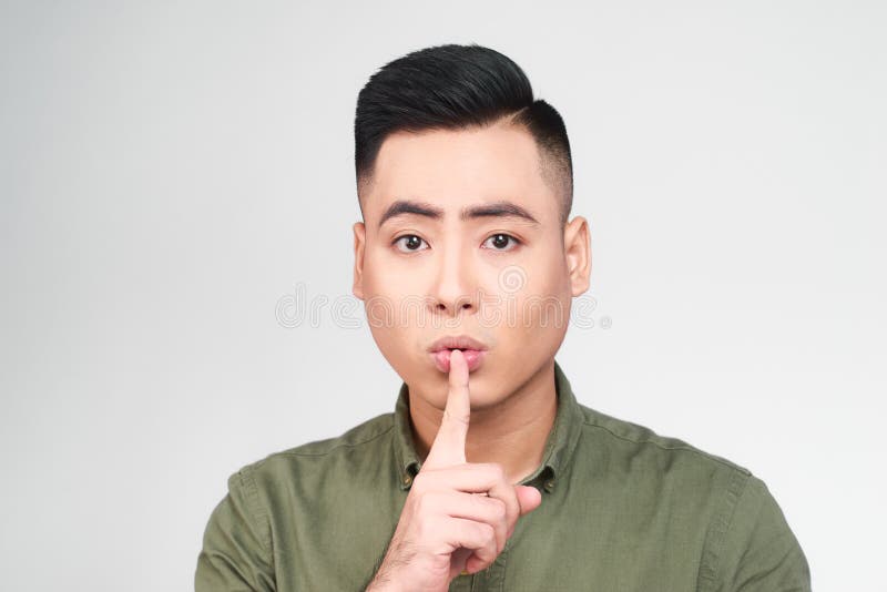 Pleasant looking delightful young male keeps finger on lips, asks not tell secret information or keep silence, isolated over gray. Background. Attractive royalty free stock image