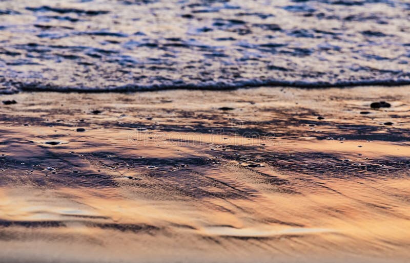Sea water edge at sunset or sunrise. Texture of waves and sand in the rays of setting sun. Copy space. Selective focus. Sea water edge at sunset or sunrise stock photo
