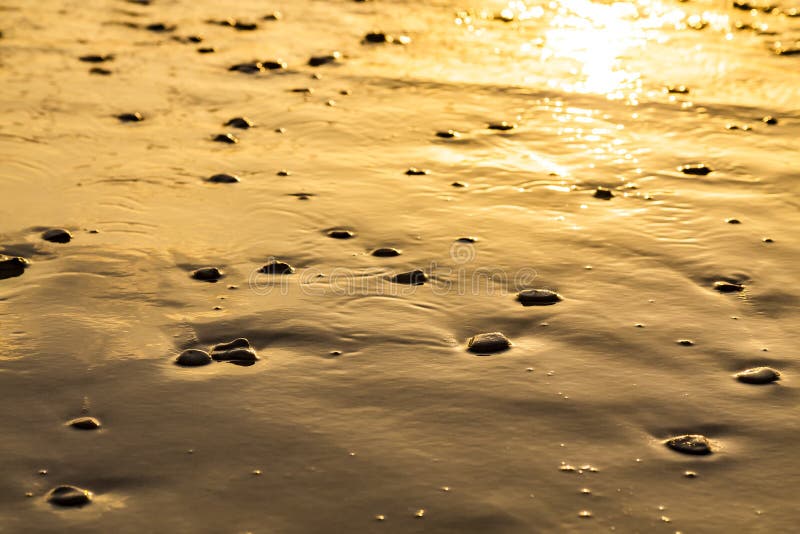 Sea water edge at sunset or sunrise. Texture of waves, wet sand and sea stones in the rays of setting sun. Copy space. Sea water edge at sunset or sunrise on the stock photo