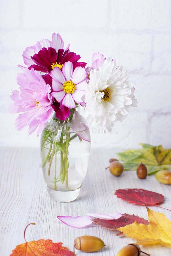 A small vase with autumn flowers is on the table with yellow and red leaves and fallen acorns. stock photo