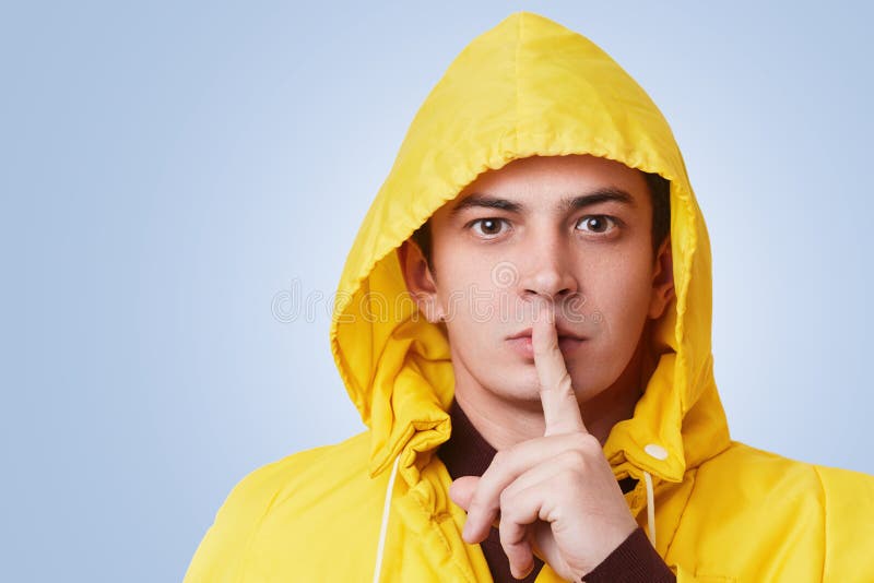 Studio shot of secret handsome pleasant looking male keeps index finger on lips, asks to keep secret and not tell secret to anybod. Y, has serious expression stock image
