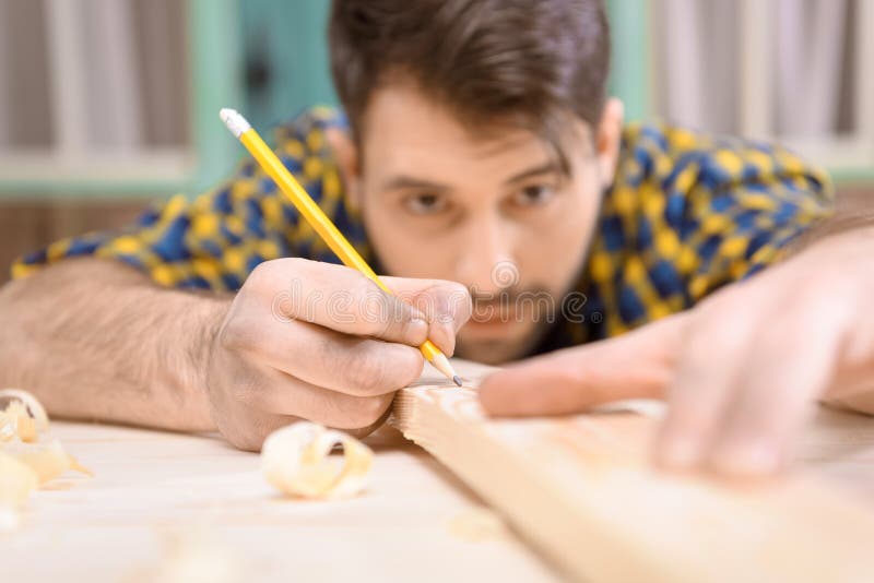 Young carpenter with pencil measuring and marking wooden plank royalty free stock photo