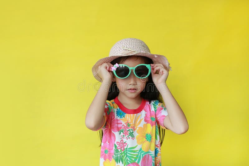 Young child girl in summer dress and hat wearing a sun glasses over yellow background with copy space.  stock photography