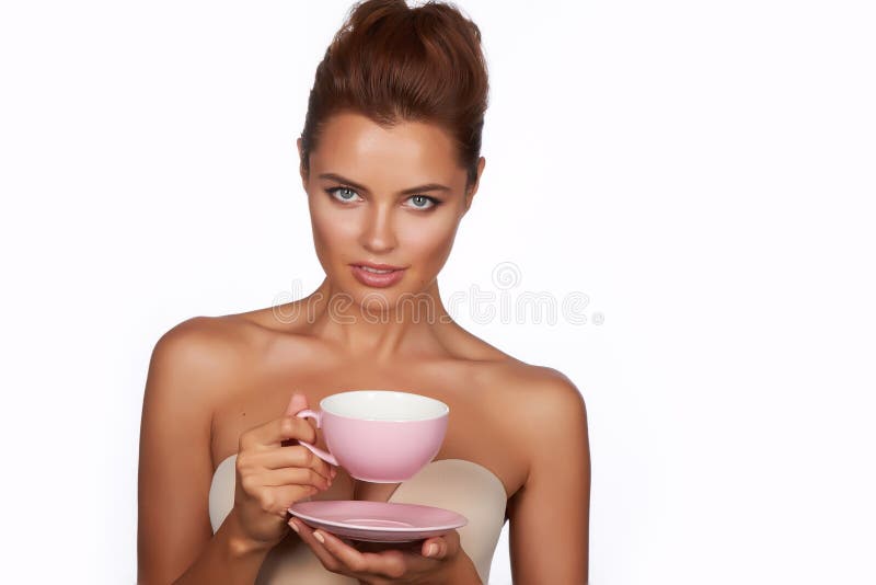 Young beautiful woman with dark hair picked up holding a ceramic cup and saucer pale pink drink tea or coffee on a white back stock photography