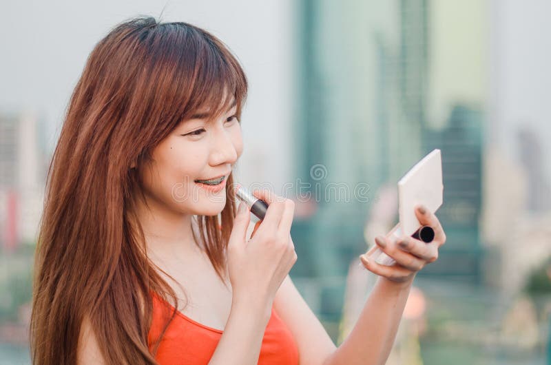 Young smiling business woman drawing lips with lipstick standing outdoors over city. Background royalty free stock photos