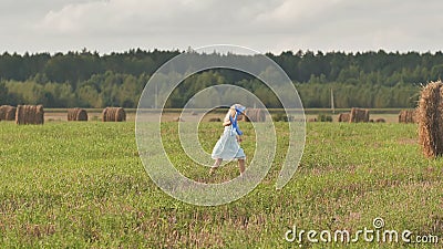A little sad girl is walking across the field with a toy airplane on a background of sheafs of straw. stock footage